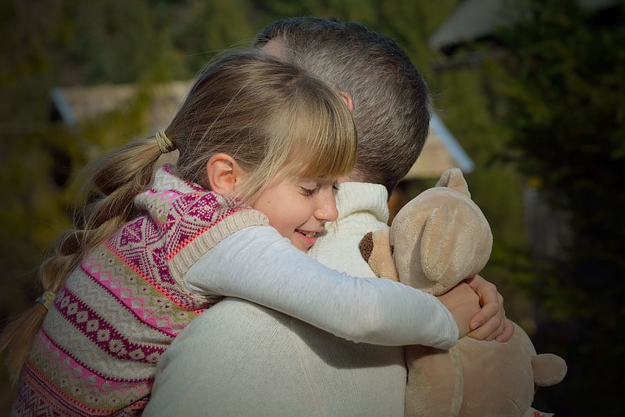 A child hugging their father. The child is also holding a teaddy bear.