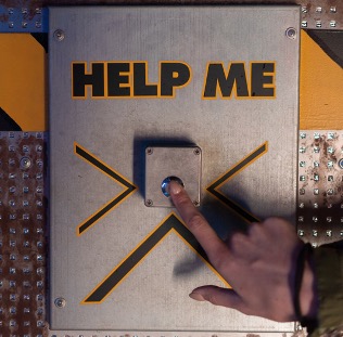 A metalic wall with a metalic button. Above the button the word 'help me' are displayed.